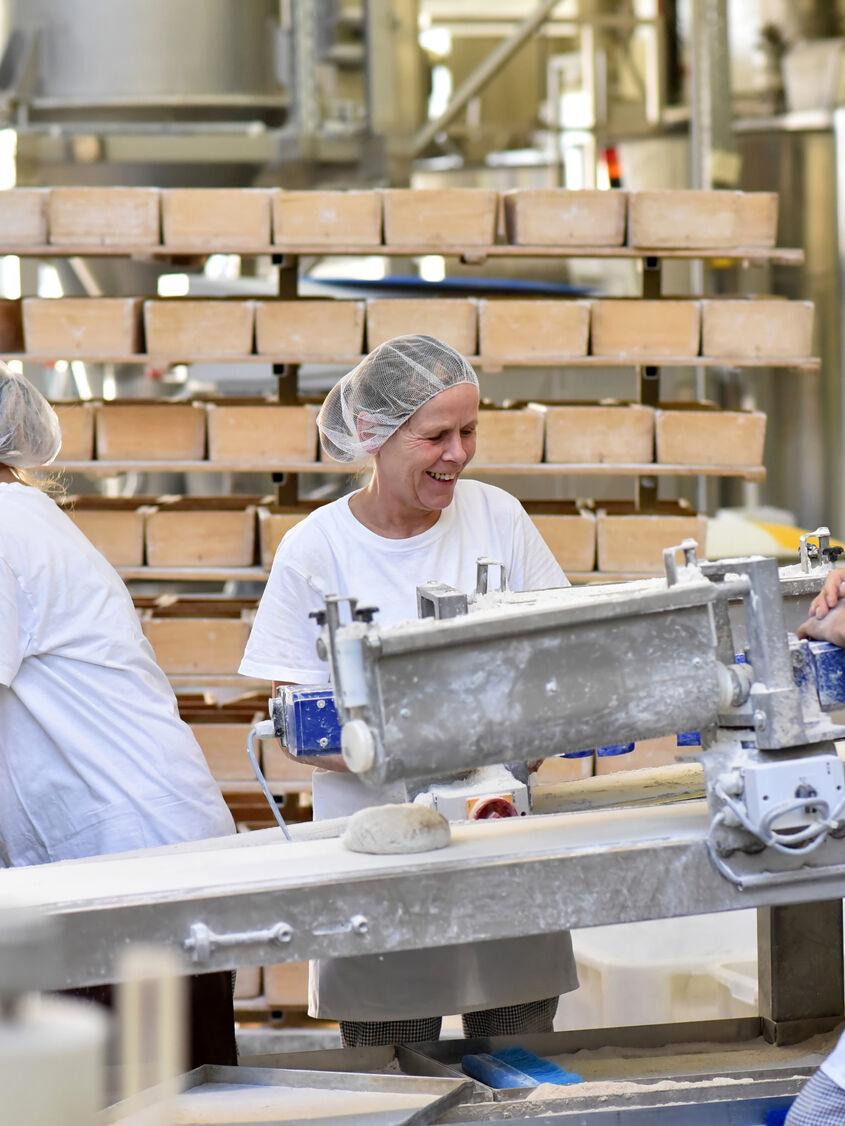 fröhliche Arbeiter bei der Herstellung von Backwaren und Broten in einer Großbäckerei // cheerful workers in the industrial production of bread in a bakery